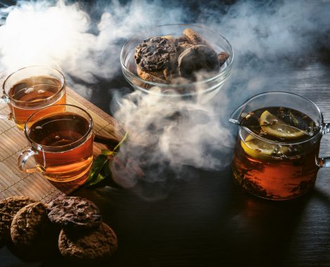 Cafe or tearoom hookah lounge concept. Two cups of aroma herbal black or red tea with some fresh cookies with spices closeup on wooden table in clouds of smoke.
